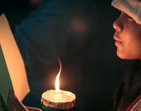 A child singing a Christmas carol by candlelight.